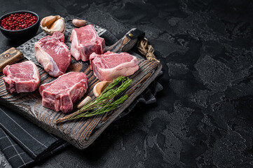 Fresh Raw lamb loin chops steaks, cutlets on butcher board with meat cleaver. Black background. Top view. Copy space - obrazy, fototapety, plakaty