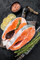 Uncooked Raw Salmon Fish Steaks on butcher board with herbs. Black background. Top view