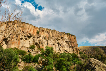 Fototapeta na wymiar Canyon photo, sun reflection and cloudscape over huge stone of canyon in ihlara valley, turkey.
