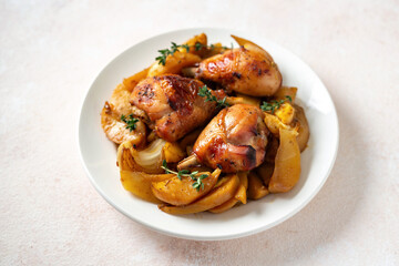 Baked chicken legs and potatoes with oranges, garlic and onions in a plate on a light culinary background closeup