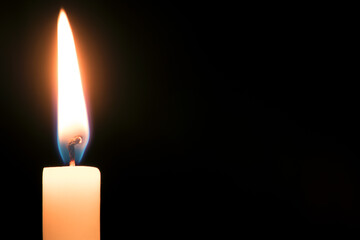 Closeup burning wax candle against black background