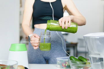 Sporty woman preparing detox smoothie after fit training in the kitchen at home.
