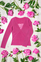 Beautiful clothing blouse in pink colors with fresh peonies flowers on light wooden background. Spring fashionable outfit, casual stylish women's clothes. Fashion concept