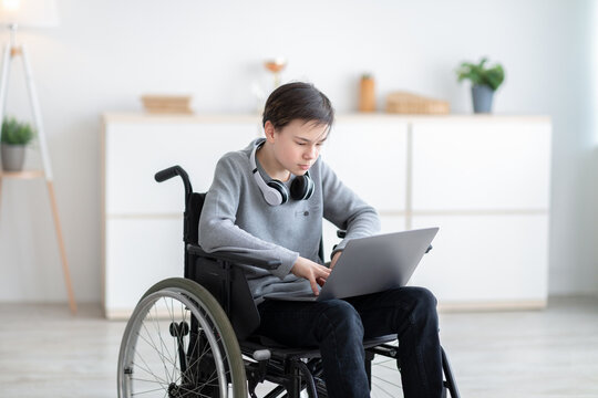Web-based education. Intelligent impaired teen boy in wheelchair having video call with tutor on laptop from home