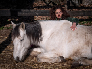 Side view of female in green polar fleece jacket creating a bond with a white pony laying down.
