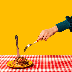 Food pop art photography. Female hand and sweet pancakes on plaid tablecloth isolated on bright yellow background. Vintage, retro style