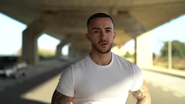 Chico joven atractivo tatuado con camiseta blanca corriendo por la carretera 