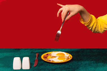 Human hand tasting bacon and eggs isolated on green and red background. Vintage, retro style interior. Food pop art photography.