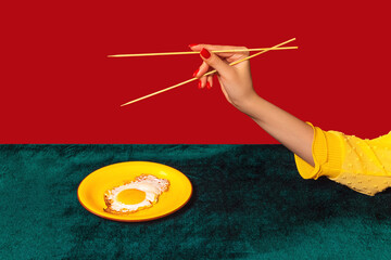 Woman's hand tasting fried eggs with chopsticks isolated on green and red background. Vintage, retro style interior. Food pop art photography.