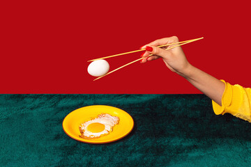 Woman's hand tasting fried eggs with chopsticks isolated on green and red background. Vintage, retro style interior. Food pop art photography.