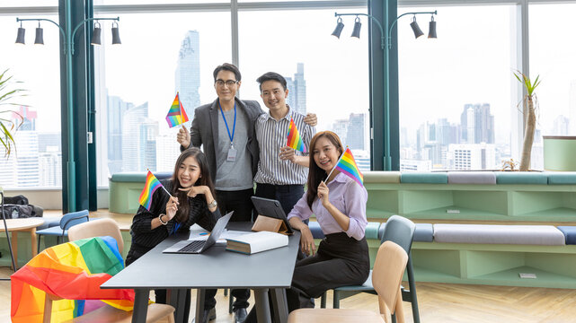 A group of construction engineers or real estate architectures from different genders and cultures with LGBT flags in their hands to support gender equity in a green office