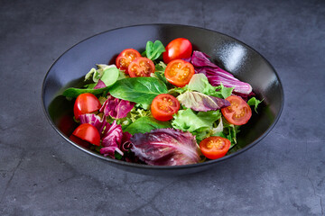 A salad of lettuce, tomato, lamb's lettuce and escarole on a black plate on a slate background