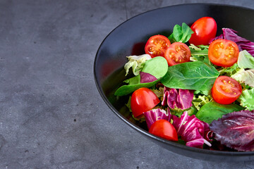 A salad of lettuce, tomato, lamb's lettuce and escarole on a black plate on a slate background