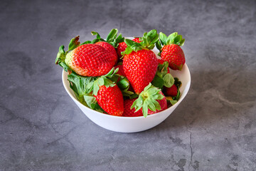 A white bowl with strawberries on a black slate background