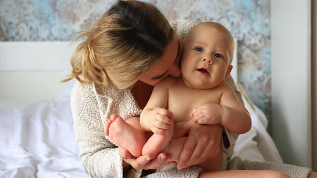mom keeps the baby at home in the bedroom. kisses him, happy motherhood, maternal love 4k
