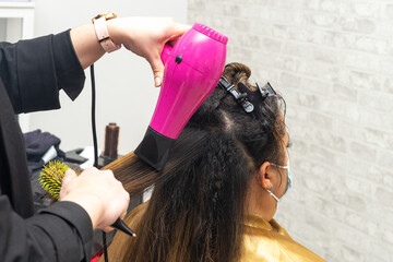 Hairdresser drying the hair of a client with damaged hair in a beauty salon using a hairdryer and a...