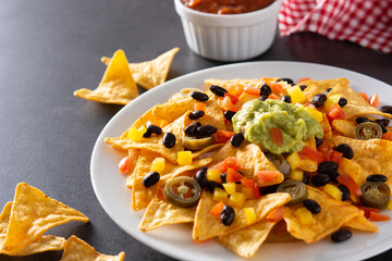 Mexican nachos tortilla chips with black beans, guacamole, tomato and jalapeno on black background