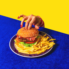 Food pop art photography. Female hand and hamburger, french fries on bright blue tablecloth isolated on yellow background. Vintage, retro style