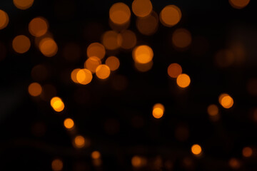 Defocused bokeh lights on black background, an abstract naturally blurred backdrop for Christmas eve or birthday party. Festive light texture. Yellow and red garland in blur. Overlay effect for design