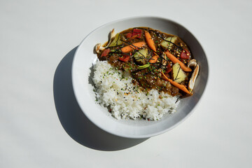 Rice topped with stir-fried ham cubes, pork, beef, and basil on white background