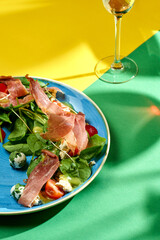 Salad with prosciutto, tomatoes, spinach and yellow dressing in a plate of bright backgrounds. Selective focus, hard shadows