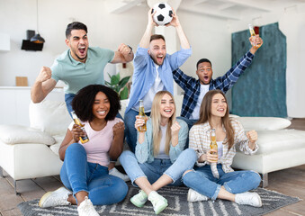 Emotional diverse friends watching soccer on TV, drinking beer, holding ball and shouting, celebrating victory at home