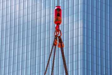 Crane hoisting block with hook on steel chain on steel rope. Glass facade of a modern skyscraper in the background. Loading\unloading of building materials on construction building site. Development.
