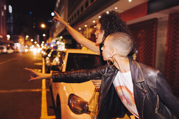 Two friends hailing a taxi in the city - obrazy, fototapety, plakaty