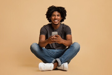 Great App. Cheerful black guy sitting on floor with smartphone in hands