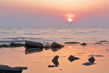 the sunset is bright over the sea on the background of rocks and reflections