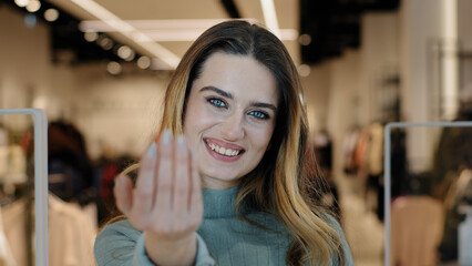Portrait caucasian female shopper seductive smiling woman saleswoman owner of clothing store looking at camera making gesture hey you come here inviting waving hand offer discount tempting approaching