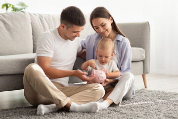 Happy Family With Little Baby Putting Coins In Piggy Bank At Home