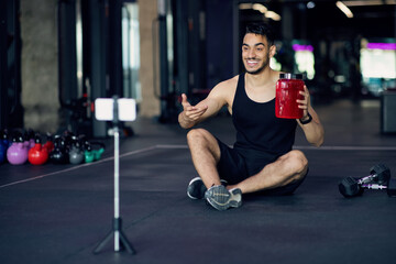 Fototapeta na wymiar Handsome Arab Fitness Blogger Recording Video Review For Sport Nutrition At Gym