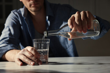 Addicted man with alcoholic drink at table in kitchen, closeup