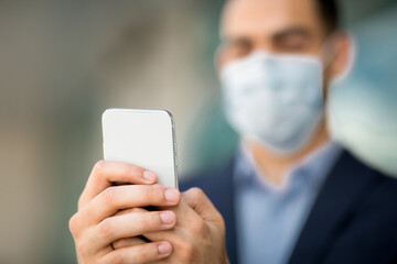Modern smartphone in unrecognizable businessman hands, man wearing face mask