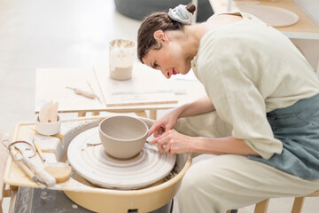 Female ceramic artist in apron working in pottery workshop