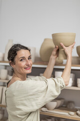 Female ceramist indoors holding handmade clay product. Conception of pottery