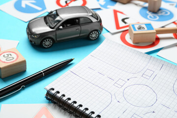Different road signs, notebook with sketch of roundabout and toy car on light blue background. Driving school