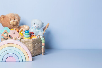 Toy box full of baby kid toys. Container with teddy bear, wooden rattles, stacking pyramid and wood blocks on light blue background. Cute toys collection for small children. Donatation. Front view