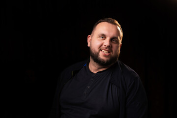 Obraz premium Portrait of a smiling young man with a beard. Dark background. Looks into the camera. Good-natured, contented, happy face.