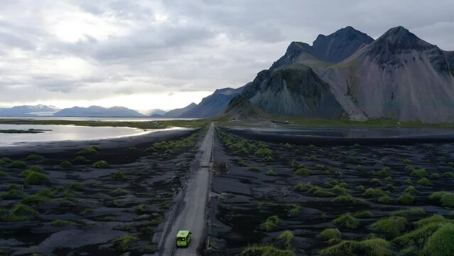 Vehicles Driving On The Road Passing Through Green Grass At Mount Vestrahorn, Stokksnes In Iceland. Aerial Shot
