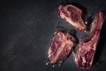Three types of steak in vacuum packaging on a dark background. Top view