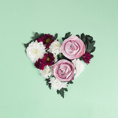 Shape of heart made of flowers and leaves on bright green background. Creative nature or Valentine concept. Minimal flat lay.