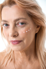 Obraz premium Serious caucasian woman with applying points of facial moisturizer while looking at camera