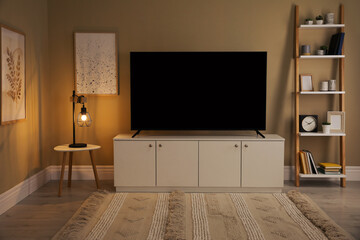 Modern TV on cabinet, white table and shelving unit near beige wall in room. Interior design