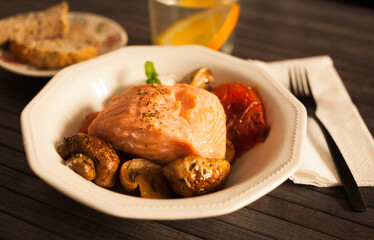 steamed salmon fillet on a pillow of fried mushrooms and tomatoes in a white bowl