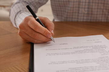 Businessman signing contract at wooden table, closeup of hands