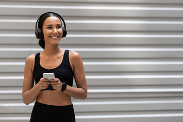 Woman In Sportswear And Wireless Headphones Resting With Smartphone After Training Outdoors