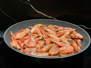 Shrimps cooked in sauce. Cooking seafood with spices, on a black background. A dish with shrimps in a frying pan.