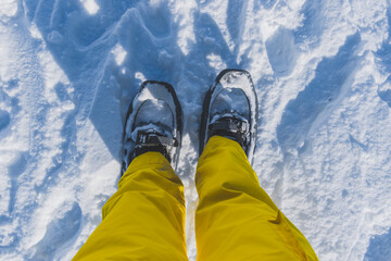 A first-person POV shot of a woman's legs in ski pants and snowshoes standing during a hike in the...